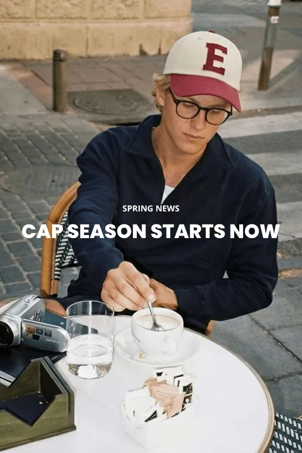 A man sits on a wooden crate in a studio wearing a classic brown felt cowboy hat with a wide brim, a dark denim shirt and jeans.